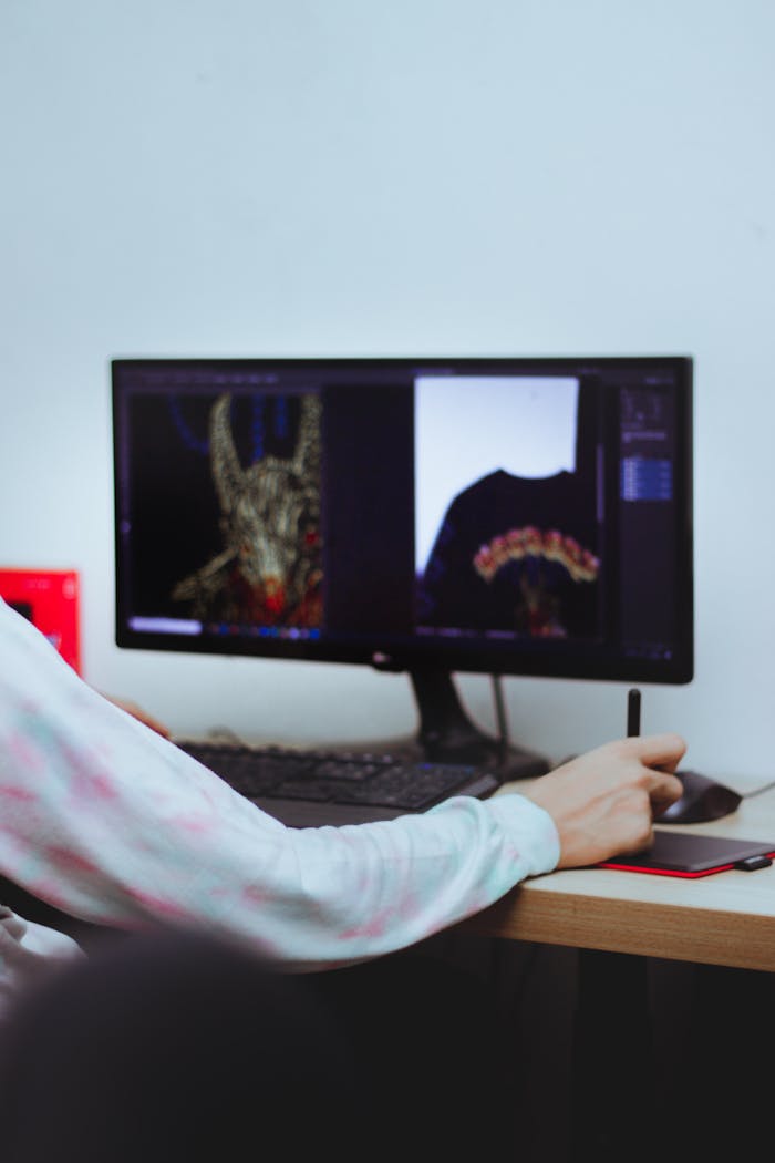 A digital artist editing designs on a computer with a stylus in an indoor workspace.